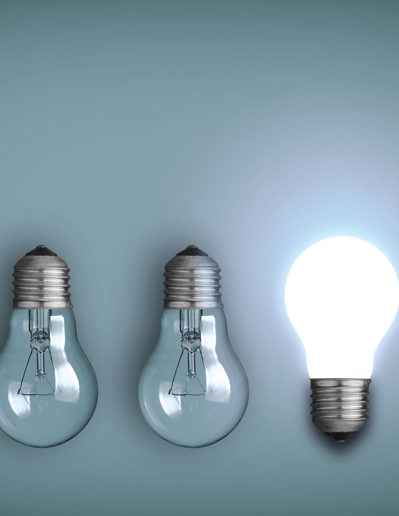 Light Bulbs The image is two light bulbs upside down and off, and one upright and on. All three are in front of a blue gray background.